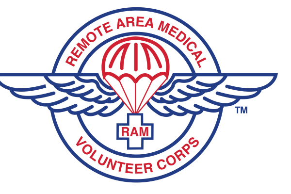 The image shows the Remote Area Medical (RAM) Volunteer Corps logo. It features a red parachute centered over a blue winged emblem, symbolizing aid delivery. The words “REMOTE AREA MEDICAL” and “VOLUNTEER CORPS” encircle the design in red text, with a cross containing “RAM” in the middle.