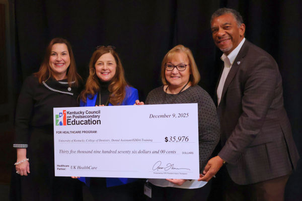 A group of four people stand smiling and holding an oversized check presented by the Kentucky Council on Postsecondary Education. The check, dated December 9, 2025, awards $35,976 to the University of Kentucky College of Dentistry for Dental Assistant/EDDA training, with UK HealthCare listed as the healthcare partner.