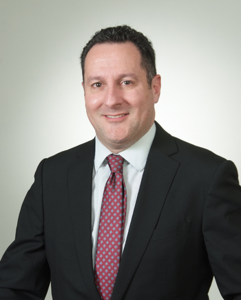 Dr. Photo of Kenneth Nusbacher in black suit jacket, white shirt, and red tie. 