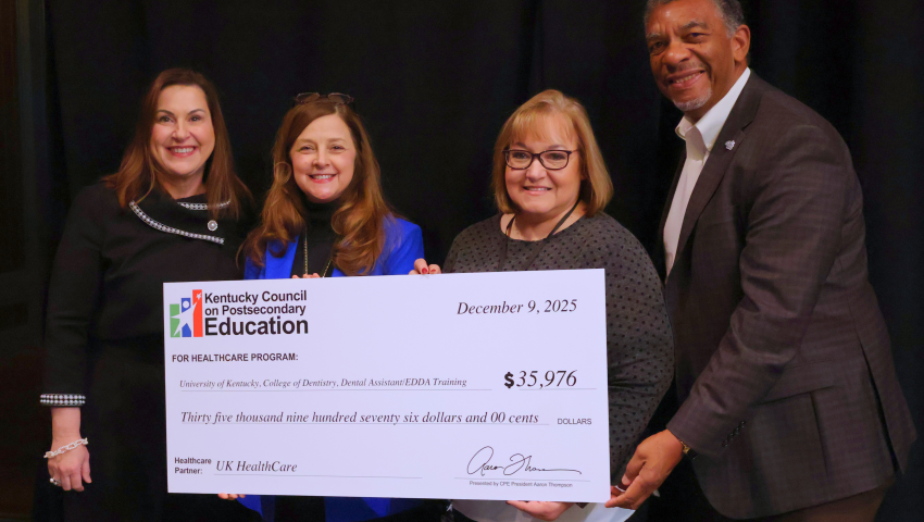 A group of four people stand smiling and holding an oversized check presented by the Kentucky Council on Postsecondary Education. The check, dated December 9, 2025, awards $35,976 to the University of Kentucky College of Dentistry for Dental Assistant/EDDA training, with UK HealthCare listed as the healthcare partner.