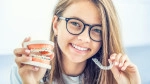 Teen girl wearing glasses holding mouth model with braces in one hand and Invisalign in the other.