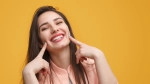 Woman smiling and pointing to her smile with two fingers. 