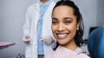 Hispanic woman smiling in a dental chair with a dental provider in the background. 
