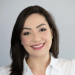 Dr. Ingrid Santamaria. A woman with medium-length dark hair and light makeup smiling, wearing a white blouse against a light gray background.
