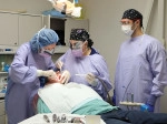 Periodontics student and staff member perform a procedure while an observer looks on.