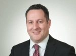 Dr. Photo of Kenneth Nusbacher in black suit jacket, white shirt, and red tie. 