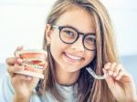 Teen girl wearing glasses holding mouth model with braces in one hand and Invisalign in the other.