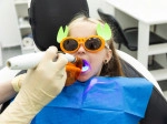 Child in dental chair with fun sunglasses and bib receiving a sealant. 