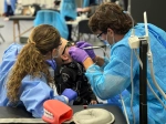 ChatGPT said:  Two dental students wearing protective gowns, masks, and gloves provide care to a young child in a dental chair. The child is wearing sunglasses, and a dental model is visible on the nearby table.