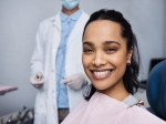 Hispanic woman smiling in a dental chair with a dental provider in the background. 