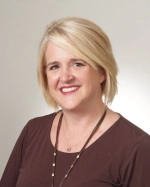 Dr. Allison Wright has blonde hair and is wearing a brown blouse and brown necklace.