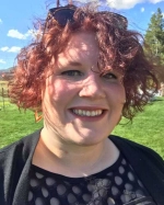 ChatGPT said:  Smiling woman with curly red hair outdoors on a sunny day, wearing a black dress.