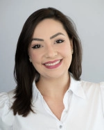 Dr. Ingrid Santamaria. A woman with medium-length dark hair and light makeup smiling, wearing a white blouse against a light gray background.
